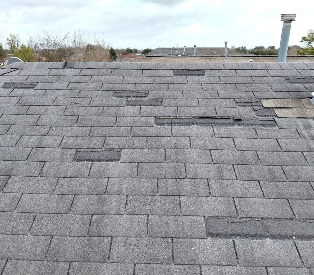 Close-up of damaged asphalt shingles with cracks and missing granules on a residential roof in Houston, Texas.