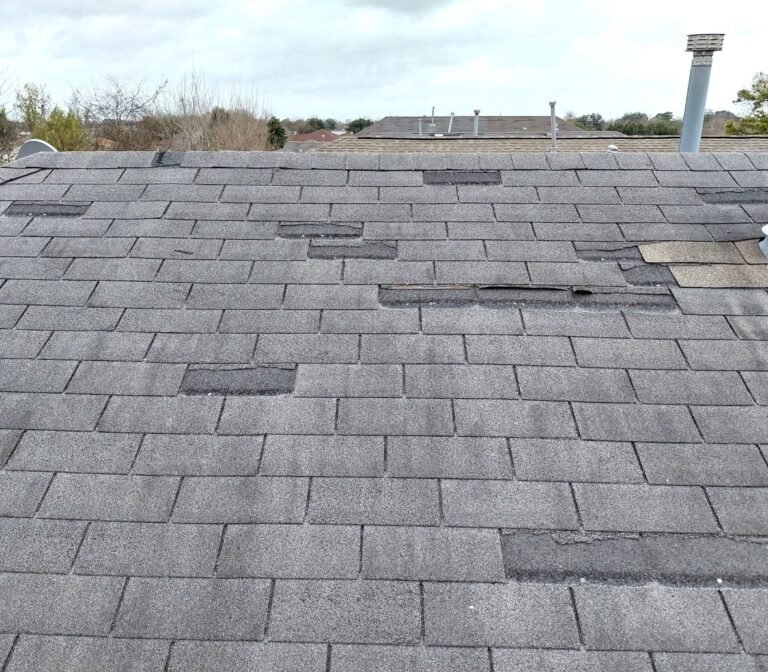 Wind damaged roof shingles with visible creasing and broken sealant strips.